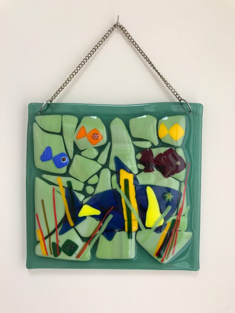 An underwater fish scene wall hanging created using cut glass that is fused together.